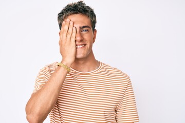 Young handsome man wearing casual clothes covering one eye with hand, confident smile on face and surprise emotion.