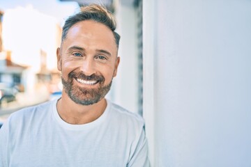 Middle age handsome man smiling happy leaning on the wall at the city.