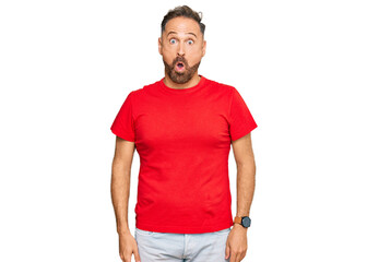 Handsome middle age man wearing casual red tshirt afraid and shocked with surprise expression, fear and excited face.