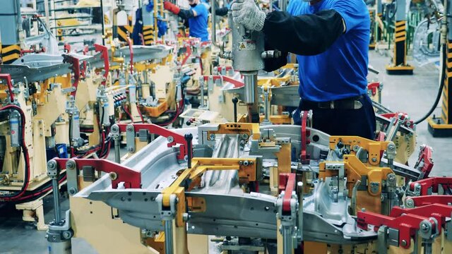 Car factory worker welding a car body part at a car factory. Automobile factory facility, car production process.
