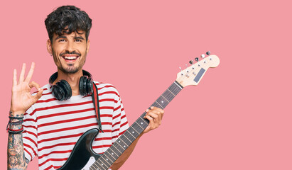 Obraz premium Young hispanic man playing electric guitar doing ok sign with fingers, smiling friendly gesturing excellent symbol