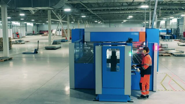Laser cutting machine is being managed by a factory employee. Laborer working with industrial equipment.