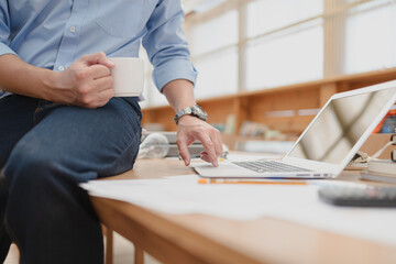 Businessman using laptop for working and hold cup of coffee in the office. Business professional concept.