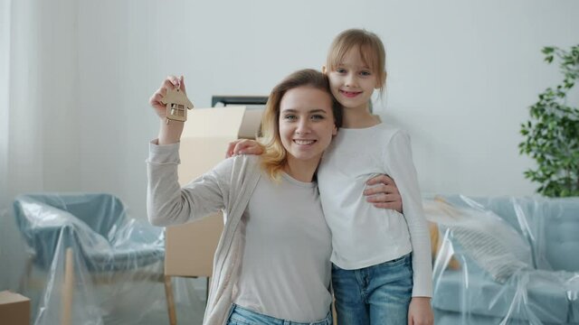 Portrait of happy young mother and little daughter smiling holding house key indoors enjoying relocation together. Motherhood and accommodation concept.