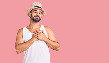 Young hispanic man wearing casual summer hat smiling with hands on chest with closed eyes and grateful gesture on face. health concept.