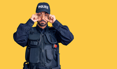 Young hispanic man wearing police uniform trying to open eyes with fingers, sleepy and tired for morning fatigue