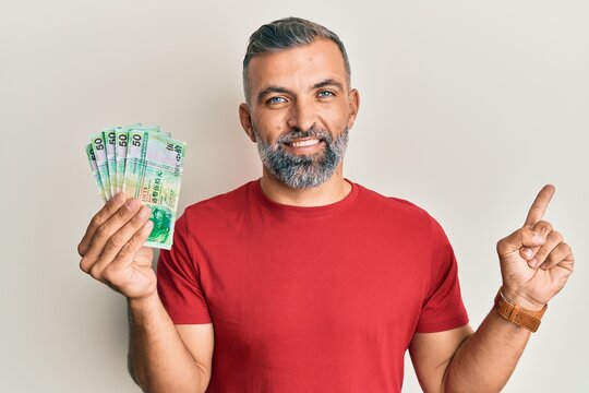 Middle age handsome man holding 50 hong kong dollars banknotes smiling happy pointing with hand and finger to the side
