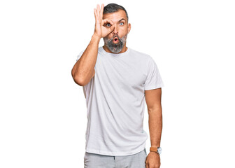 Fototapeta premium Middle age handsome man wearing casual white tshirt doing ok gesture shocked with surprised face, eye looking through fingers. unbelieving expression.