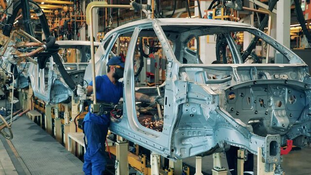 Several car factory workers using a welding machine on a car assembly line. Automobile factory interior. Industrial plant, industrial workers at, automobile factory, car production factory facility.