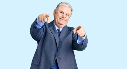 Senior grey-haired man wearing business jacket pointing to you and the camera with fingers, smiling positive and cheerful