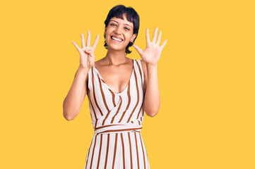 Young brunette woman with short hair wearing summer outfit showing and pointing up with fingers...