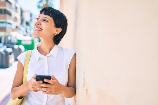 Young woman with short hair smiling happy outdoors using smartphone
