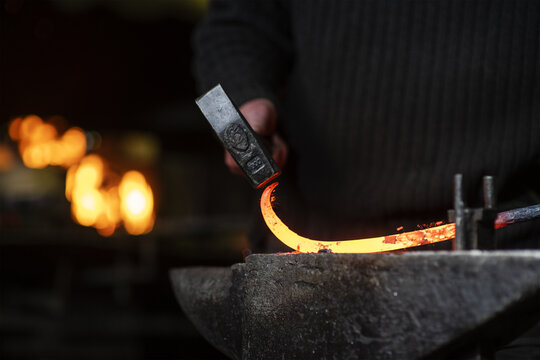 A close-up image of a blacksmith's hands forging a spiral from a red-hot billet against the background of a forge. Handicraft concept