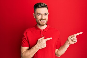 Young redhead man wearing casual clothes smiling and looking at the camera pointing with two hands and fingers to the side.