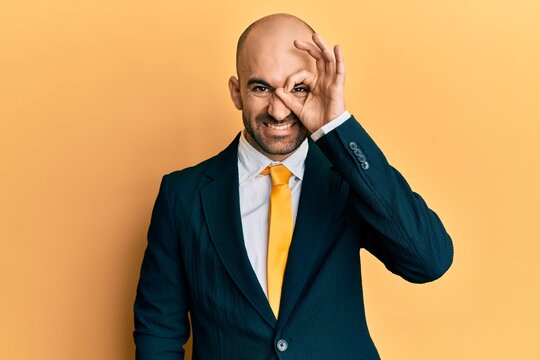 Young hispanic man wearing business suit and tie doing ok gesture with hand smiling, eye looking through fingers with happy face.
