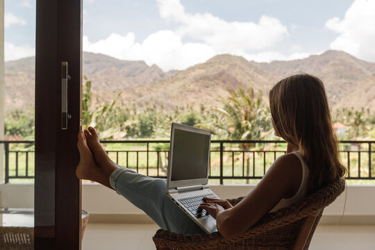Freelancer, remote work, work from home. Young woman is working on a laptop on her balcony overlooking the ropical garden