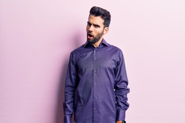 Obraz premium Young handsome man with beard wearing casual shirt in shock face, looking skeptical and sarcastic, surprised with open mouth