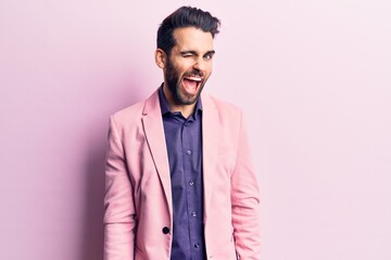 Young handsome man with beard wearing elegant jacket winking looking at the camera with sexy...