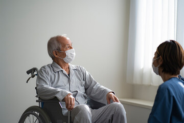 マスクをつけて車椅子に座る日本人シニア男性と看護師