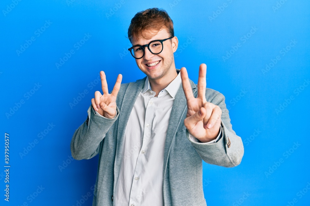 Wall mural Young caucasian man wearing elegant clothes and glasses smiling looking to the camera showing fingers doing victory sign. number two.