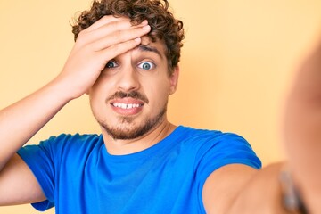 Fototapeta na wymiar Young caucasian man with curly hair wearing casual clothes taking a selfie stressed and frustrated with hand on head, surprised and angry face