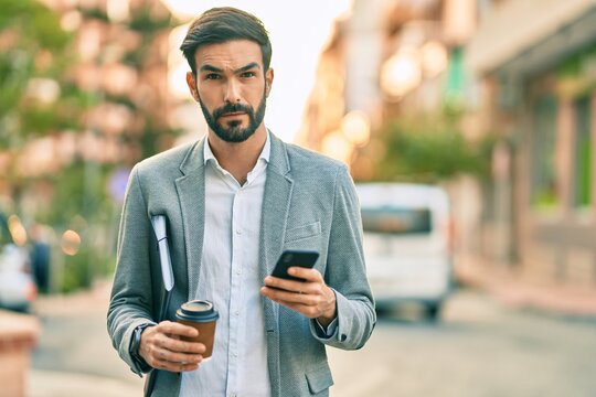 Young hispanic businessman with serious expression using smartphone and drinking coffee at the city.