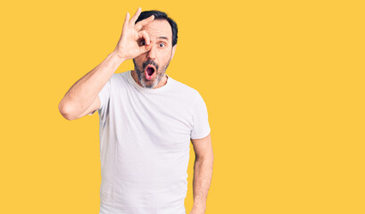 Middle age handsome man wearing casual t-shirt doing ok gesture shocked with surprised face, eye looking through fingers. unbelieving expression.