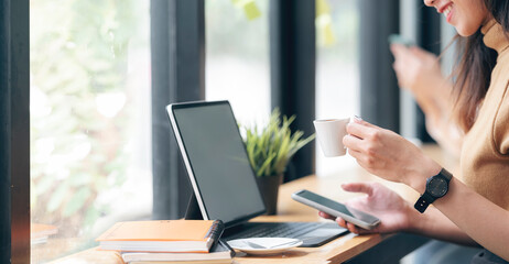 Cropped image of female hands holding cup of coffee and using smartphone while sitting at cafe.