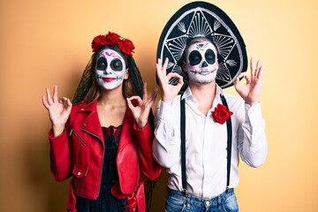 Couple wearing day of the dead costume over yellow relax and smiling with eyes closed doing meditation gesture with fingers. yoga concept.