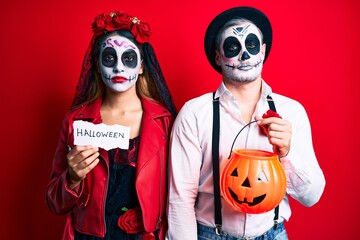 Couple wearing day of the dead costume holding pumpking and halloween paper relaxed with serious expression on face. simple and natural looking at the camera.
