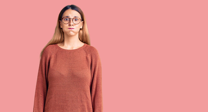 Beautiful young woman wearing casual clothes and glasses puffing cheeks with funny face. mouth inflated with air, crazy expression.