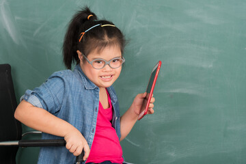 Portrait of young Asian disabled child down's syndrome girl student in happy and smile emotion using tablet for education in front of chalkboard in element classroom