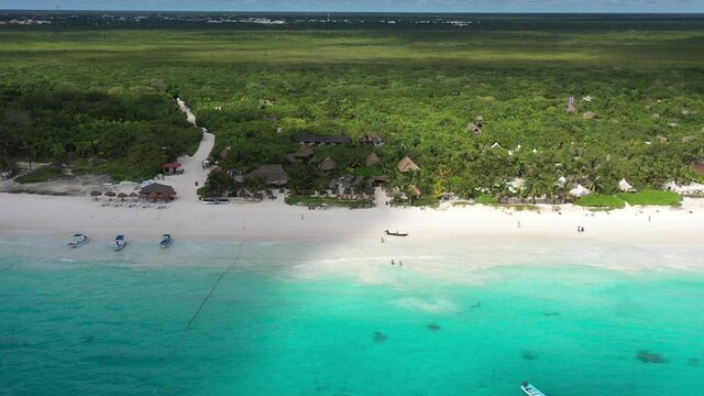 Vista a&eacute;rea panor&aacute;mica de la densa jungla tropical que rodea la playa en Tulum, M&eacute;xico. El drone volando de forma lateral con un mar azul turquesa.