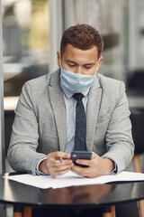 Businessman in a city. Person in a mask. Coronavirus theme. Guy with documents and phone;