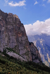 Summer view on a steep rocky slope of a mountain in a majestic gorge with white clouds in blue sky