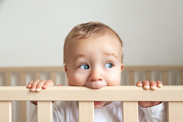 Blond cute little baby biting wooden bed headboard