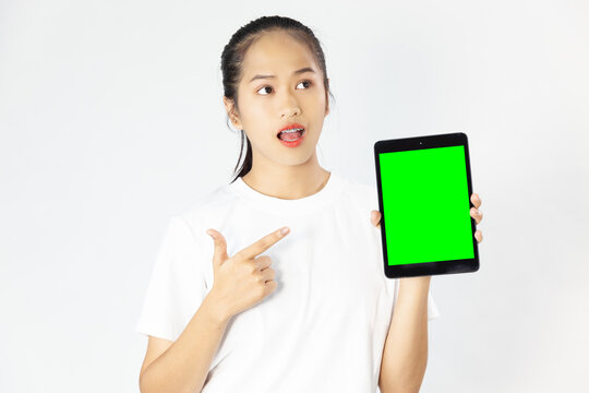 Young pretty woman in white shirt pointing finger to blank green screen tablet for your write a content on the white studio background