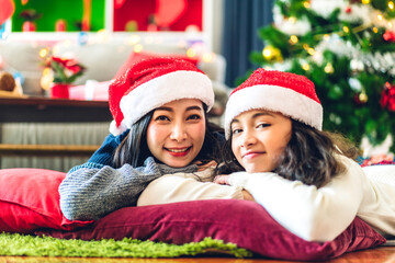 Portrait of happy asian family mother with daughter in santa hats having fun look at camera and enjoying spending time together in christmas time at home