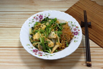 Fried and stirred instant noodle mixed with vermicelli and local herbal vegetable on the plate. Fusion vegetarian menu in Asia restaurant. 