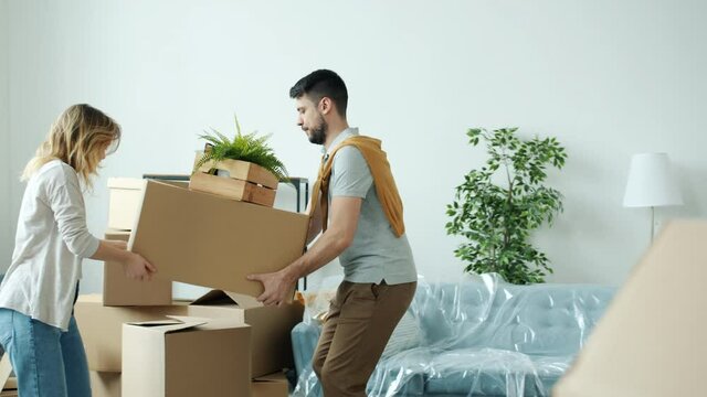 Slow motion of girl and guy happy couple moving boxes carrying belongings relocating to new apartment together. Accommodation and relocation concept.