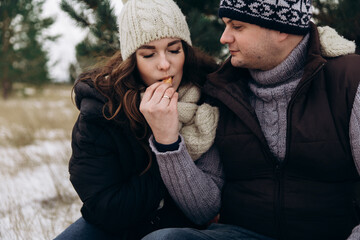 A man treats a young woman to a tangerine. The man has a ring on his finger. People are dressed in dull winter clothes. Christmas trees can be seen in the background. High quality photo