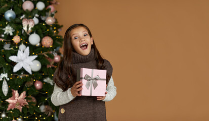 cute joyful little child girl holding Christmas gift box in hand on background of christmas tree. copy space