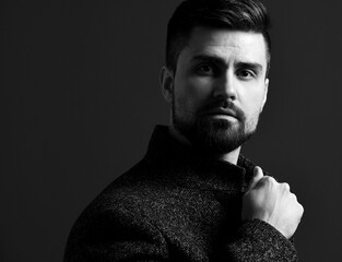 Black and white portrait in profile of serious bearded businessman holding his stylish tweed jacket looking at camera