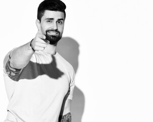 Portrait of cheerful brutal bearded man fun guy with tattoo on arms in white t-shirt pointing finger at camera shooting and winks over white background. Hipster stylish look for free lifestyle concept