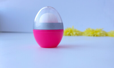 Hygienic lipstick closed in a pink bottle, minimalism. Isolated close-up view of a closed white lipstick with a transparent cap suitable for branding with corporate logos and advertisements.