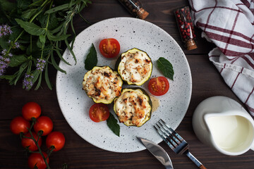 Baked stuffed zucchini columns with minced chicken and vegetables on a plate. Dark wooden background.