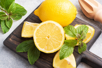 Juicy yellow lemons whole and cut with fresh mint leaves on a wooden stand. Close up.