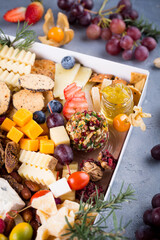 Fototapeta na wymiar Cheese plate with delicious snacks. Christmas gift box with assorted cheese cubes, meat slices, fruits and nuts in gift box with crackers, olives and wine glass. Delicious charcuterie, copy space