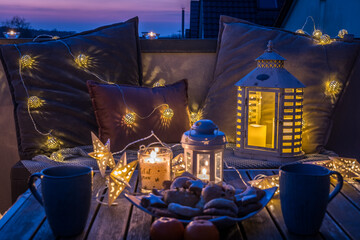 Cozy sitting area with coffee and cookies on a balcony, decorated for winter with lanterns,...