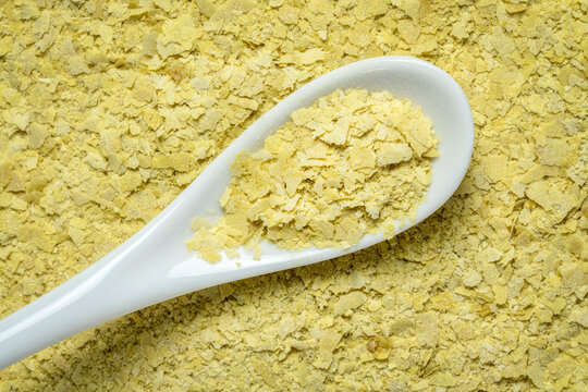 closeup of nutritional organic yeast flakes - background and texture with a white teaspoon, nutrition supplement, baking and cooking